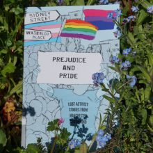 Prejudice and Pride Cover Blue background, an activist holds a sign 'Prejudice and Pride' rainbow flag, signposts to Sidney Street and Waterloo Place